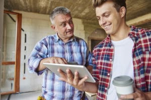 Worker and young man at construction site in home on tablet