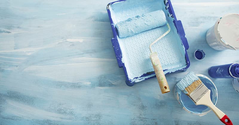a painting roller in blue paint and a pan