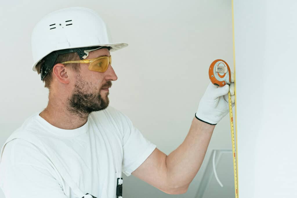 Contractor measuring a wall with a tape measure during work experience for a home improvement license.