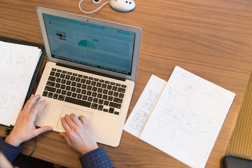 A contractor reviewing digital project details on a laptop alongside printed plans during estimating.