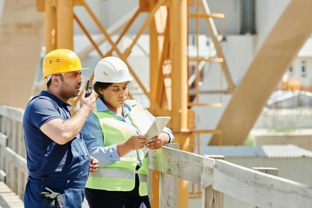 Construction supervisor and project manager reviewing jobsite details on a tablet during coordination.