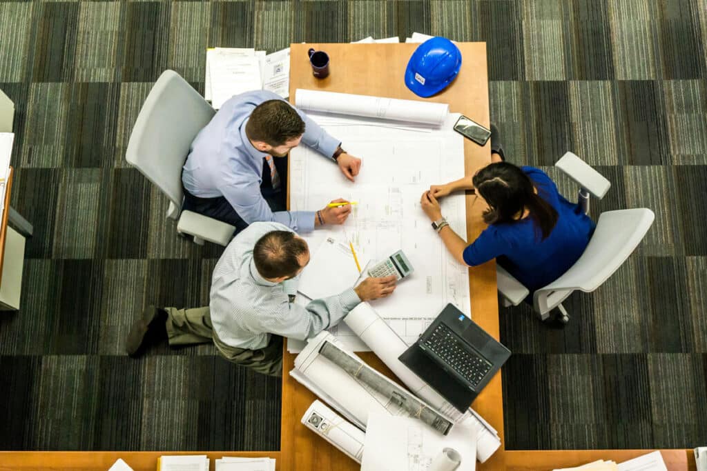 Team reviewing construction blueprints at a desk with plans, a laptop, a calculator, and a safety helmet.