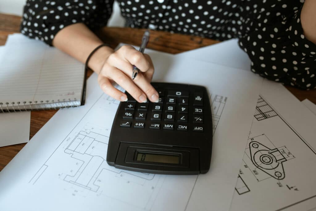 Contractor using a calculator on top of printed construction blueprints with a notebook and pen for estimates.