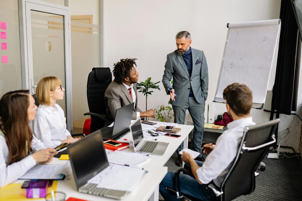 Coworkers collaborating at a table with laptops open while discussing their tasks and business workflow.