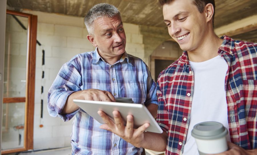 Worker and young man at construction site in home on tablet